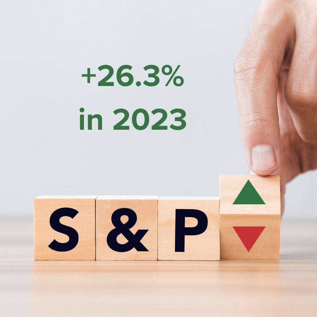 Wooden blocks on a wooden table which say 'S', '&', and 'P' in black. Another block with a green up arrow and a red down arrow are being held up on an edge by a hand. Green text at the top says '+26.3% in 2023'