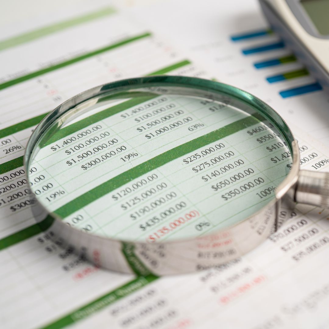 Magnifying glass on a spreadsheet with dollars along with a calculator