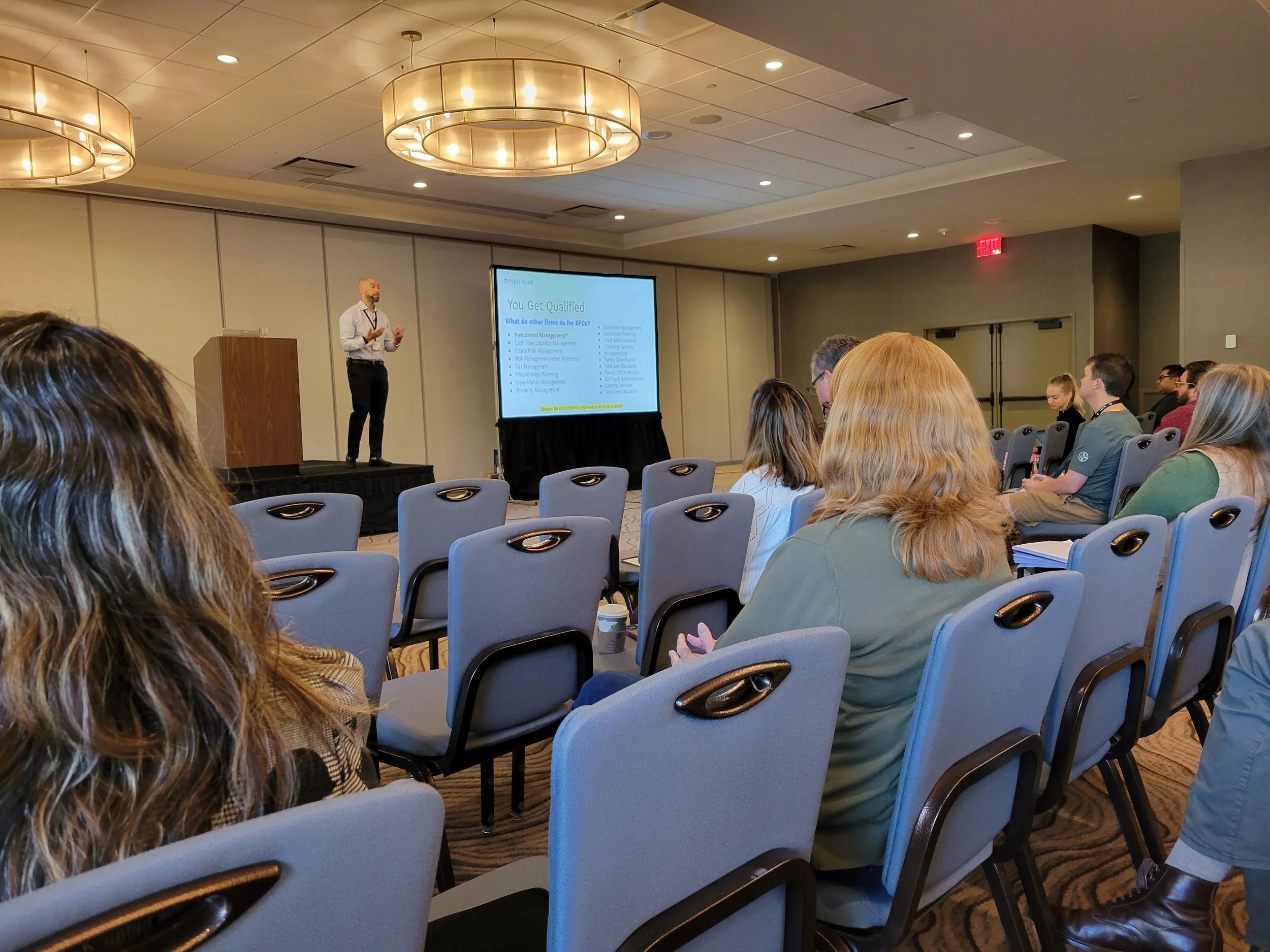 Photo of Jason Howell presenting to a crowd in the front of a large hotel conference room.