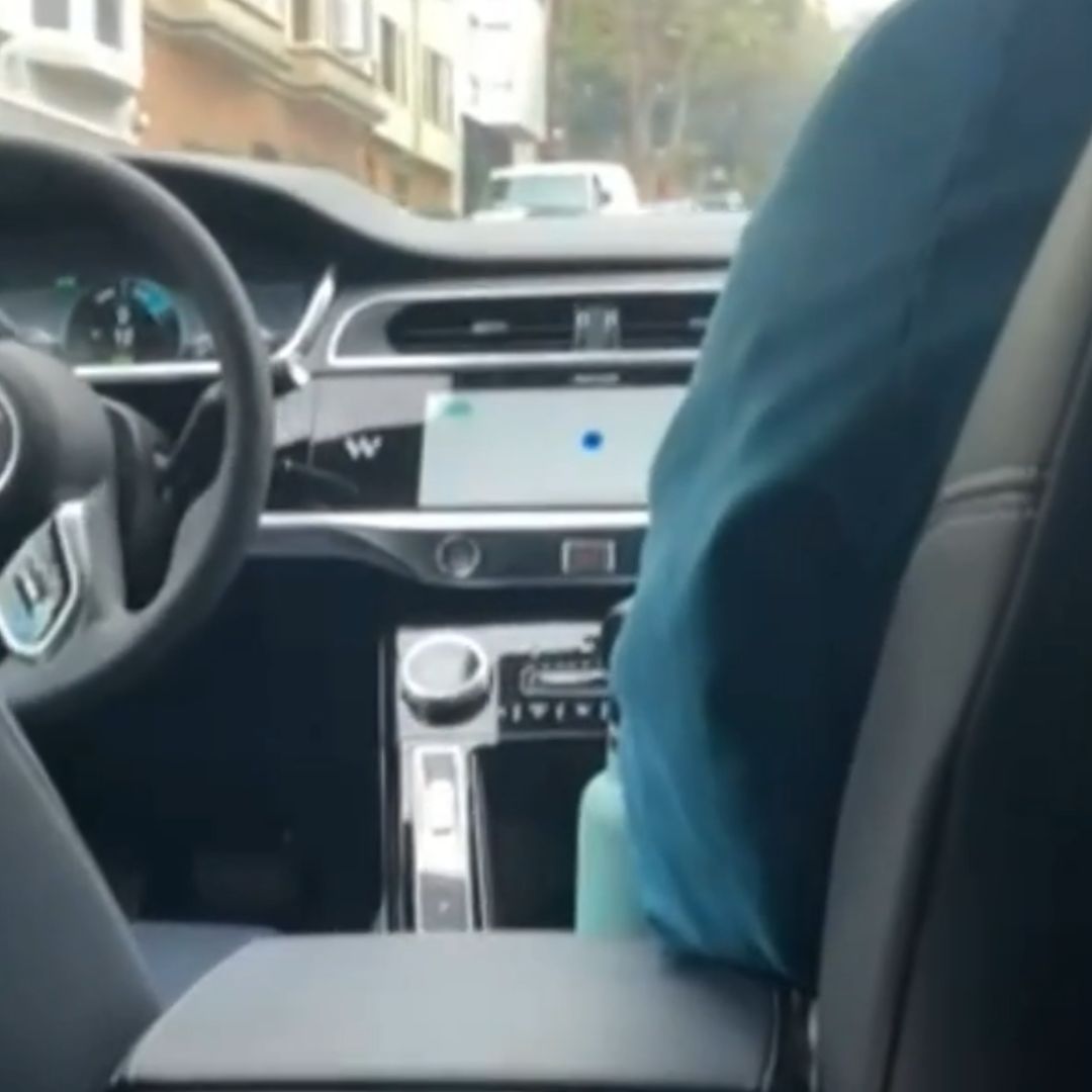 It's the interior of a vehicle. The interior is black leather with a shiny display. Someone sits in the front passenger side but there's no driver.