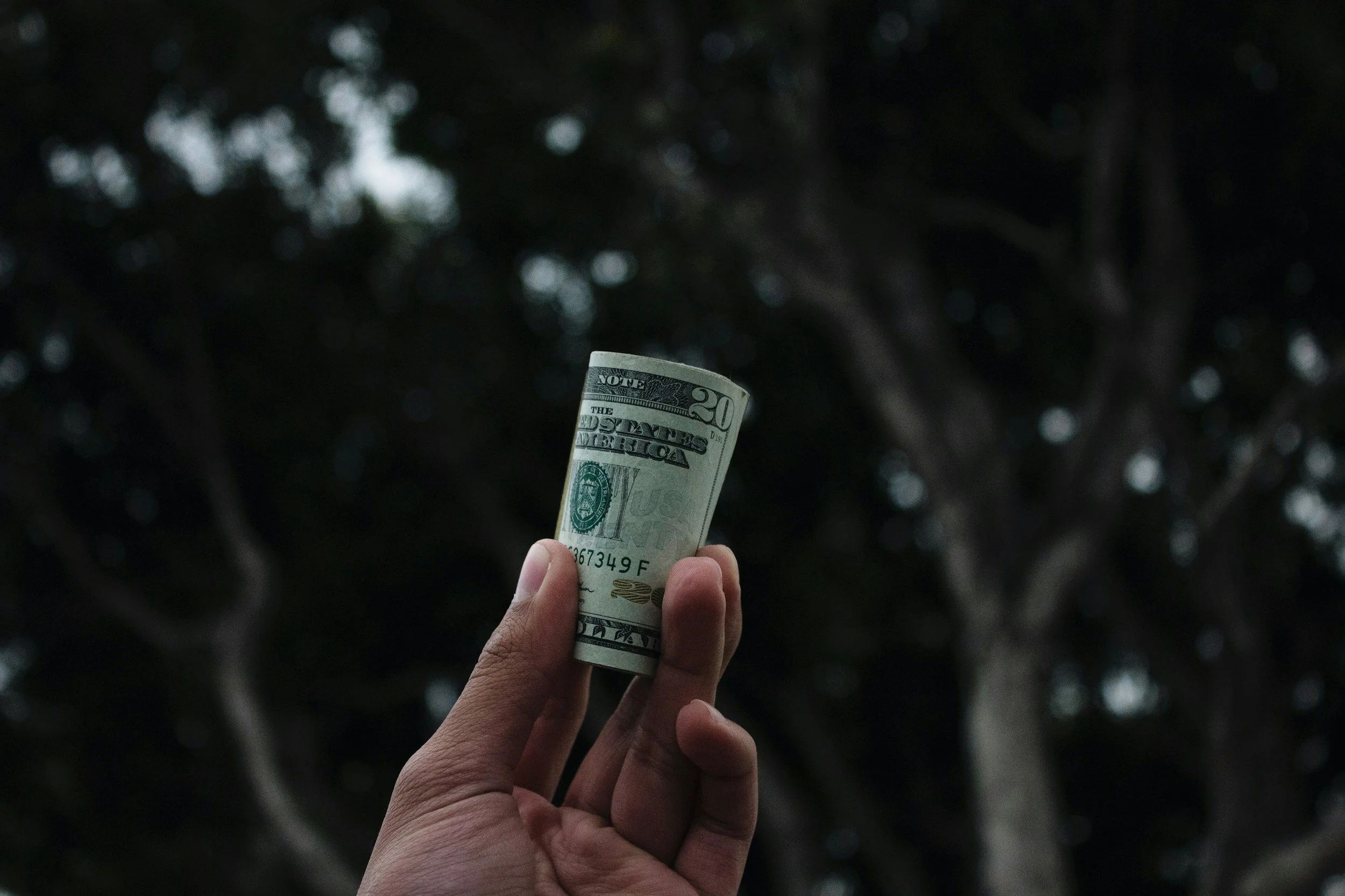 Close up of a roll of $20 bills in a person's hand.