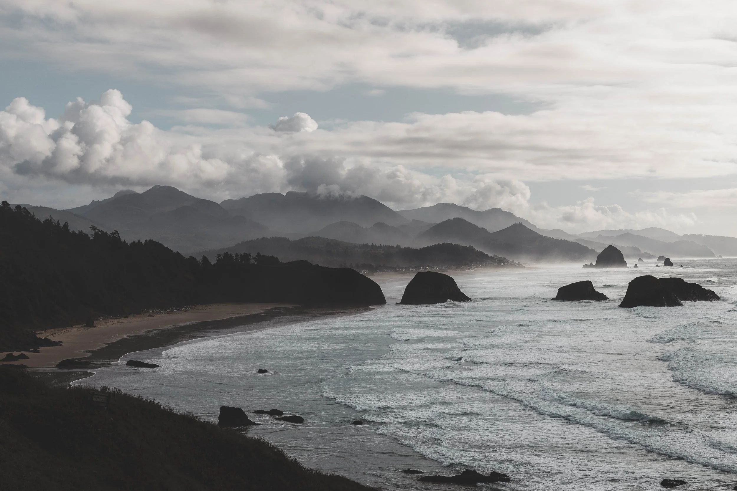 A gray and misty ocean shoreline featuring a small mountain range.